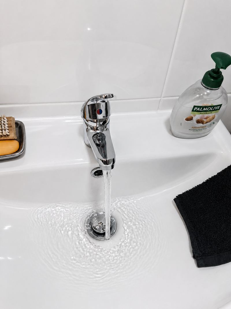 Chrome basin mixer tap running into a white bathroom basin, with hand soap and a dark towel beside it