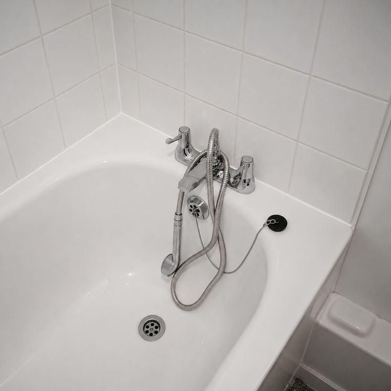 Chrome bath mixer tap with a coiled shower hose and handset resting in a white bath against white tiles